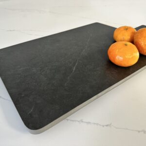 Cutting board with three oranges on a marble countertop.