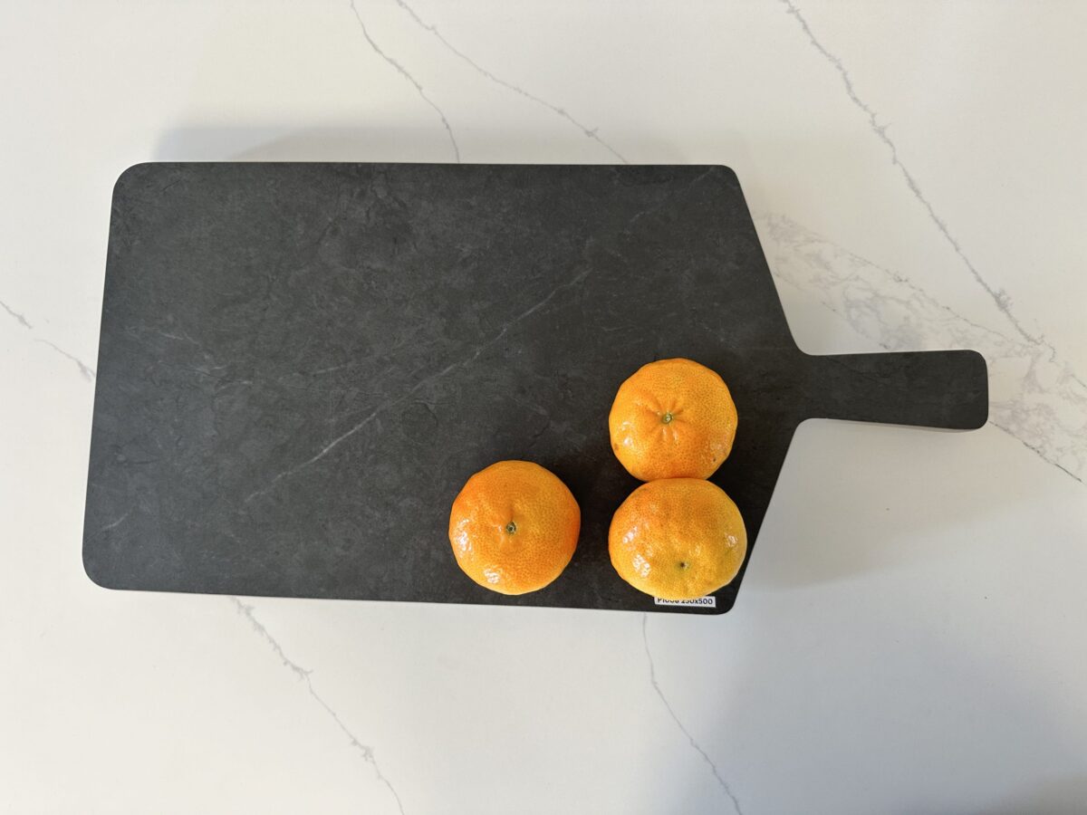 Three oranges on a black cutting board on a marble countertop.