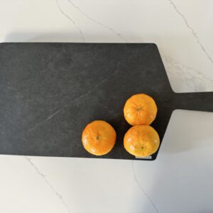 Three oranges on a black cutting board on a marble countertop.
