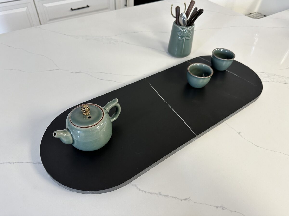 Ceramic teapot and cups on a black serving tray in a kitchen.