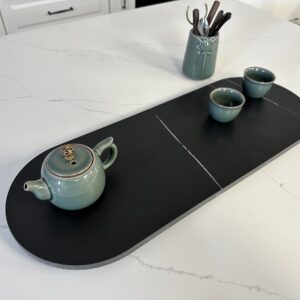 Ceramic teapot and cups on a black serving tray in a kitchen.