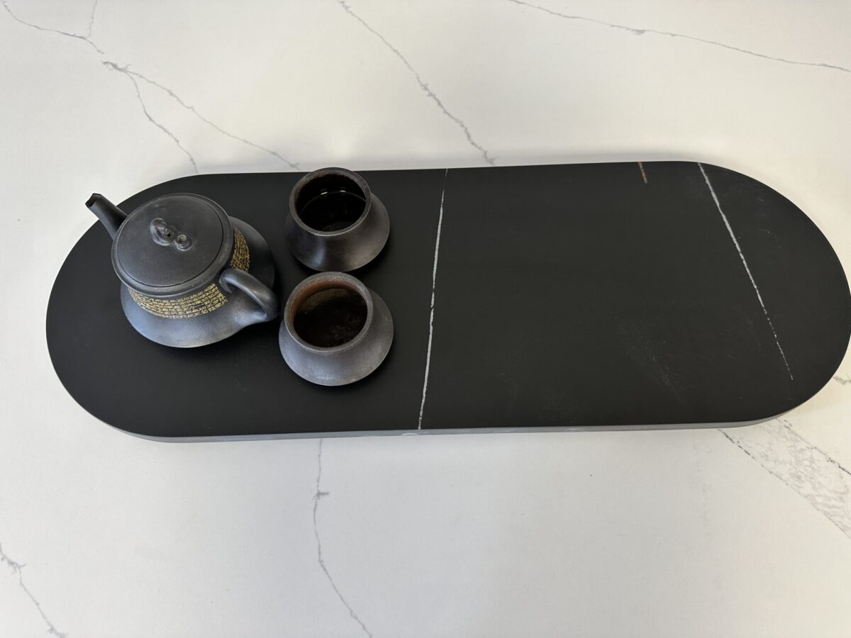 Black teapot and cups on a dark serving tray.