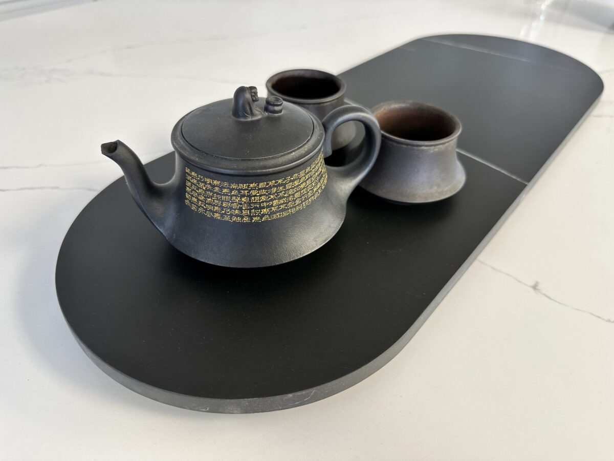 Black teapot and cups on a sleek black tray.