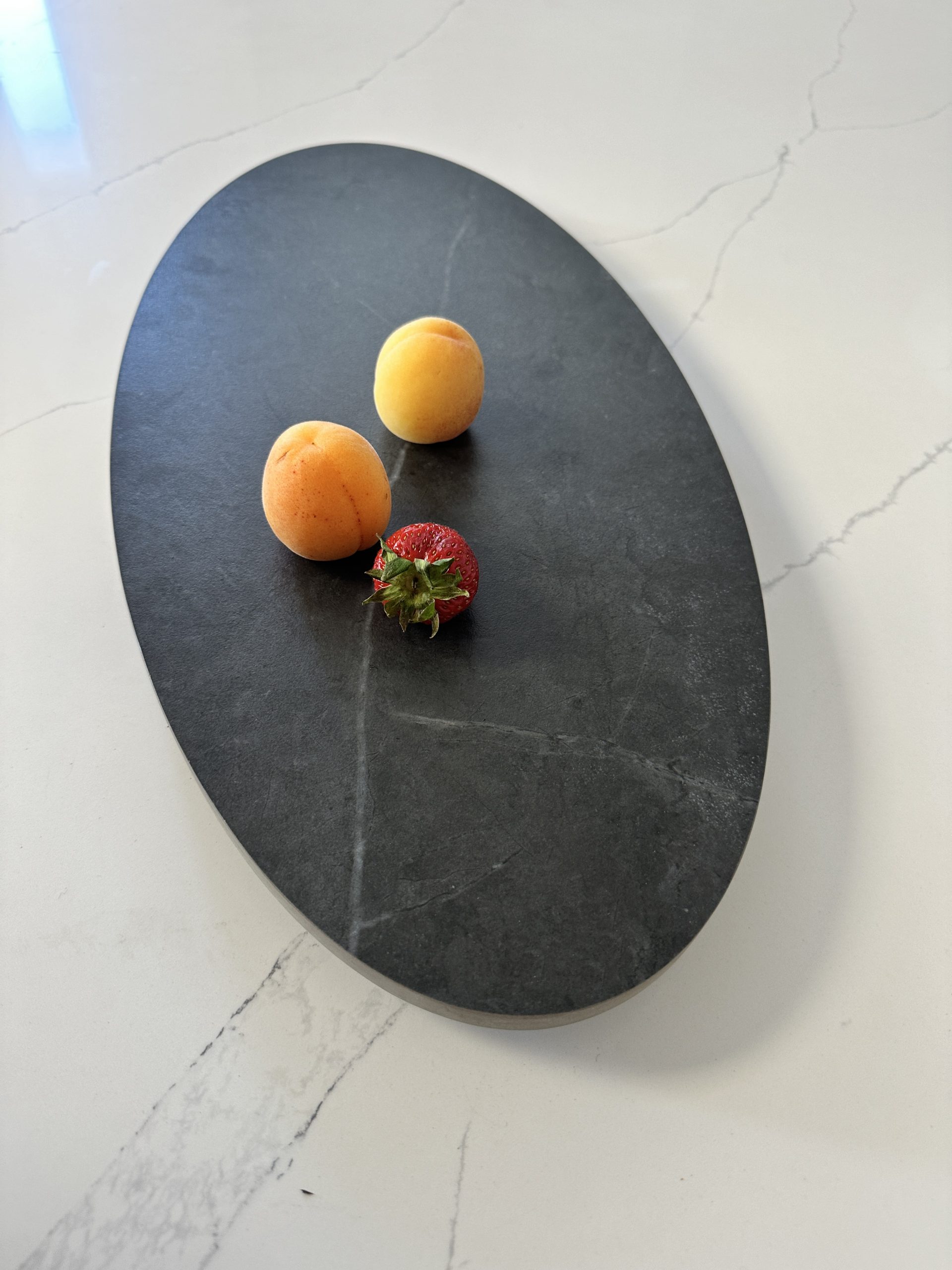 Two apricots and a strawberry on a dark oval platter.