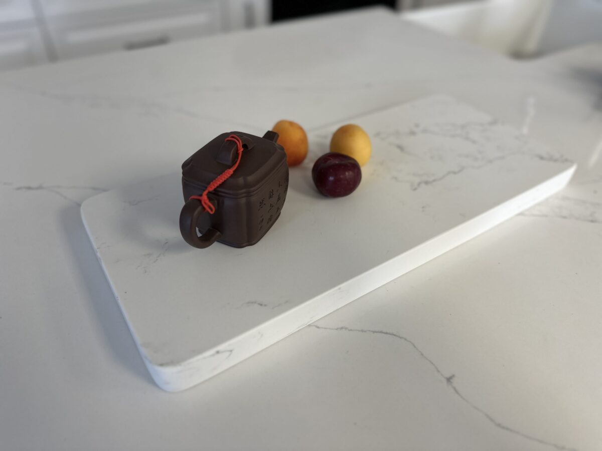 Teapot and fruit on a white marble cutting board.