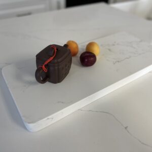Teapot and fruit on a white marble cutting board.
