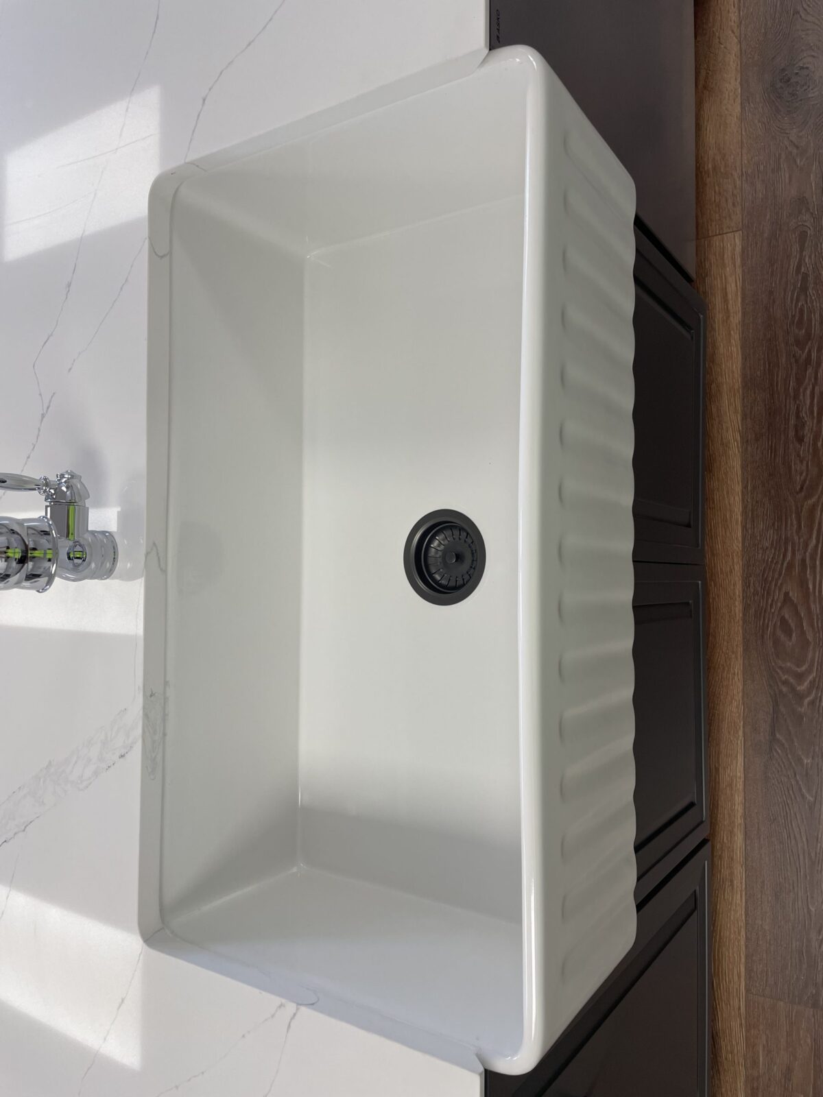 White kitchen sink with black drain, marble countertop, and wooden floor.
