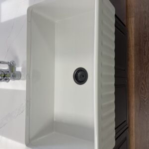 White kitchen sink with black drain, marble countertop, and wooden floor.