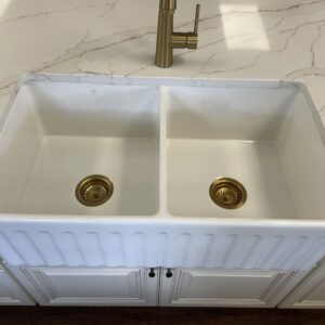 White double kitchen sink with brass fixtures on marble countertop.
