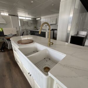 Modern kitchen with marble countertops, farmhouse sink, and gold faucet.