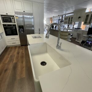 Modern kitchen with white countertops, large sink, and stainless steel appliances.