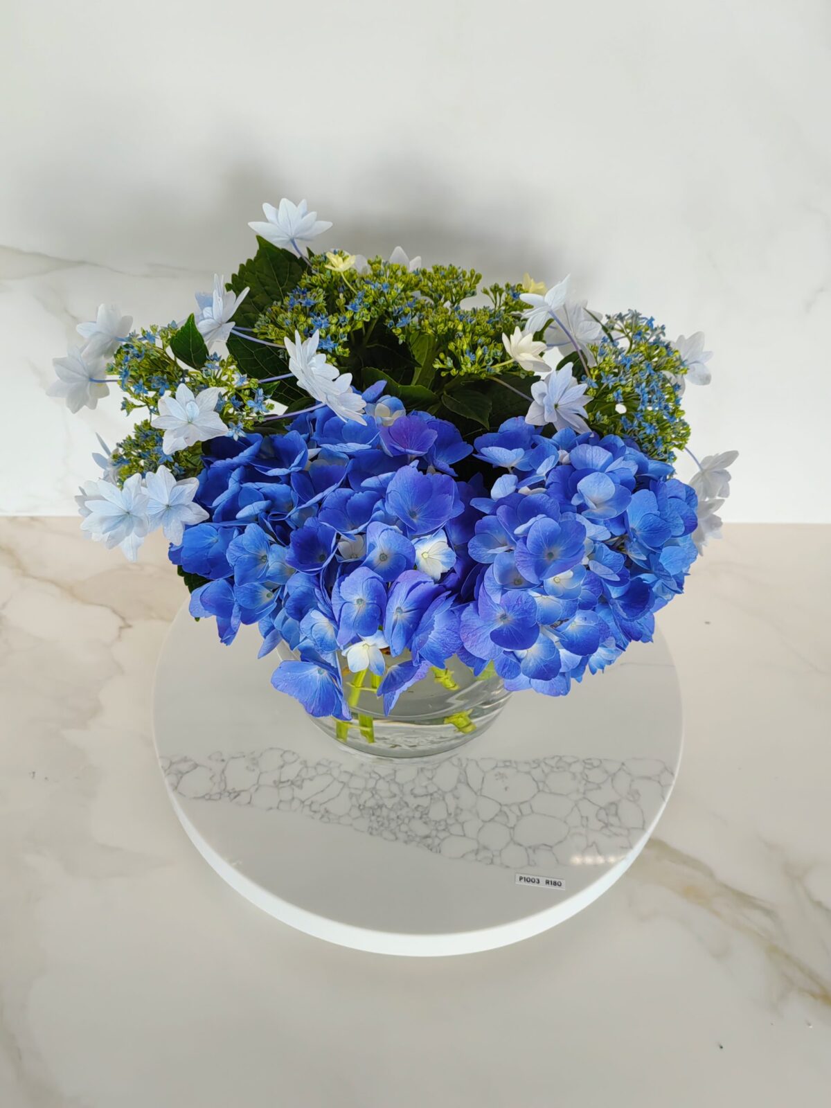 Blue and white hydrangea bouquet in a glass vase on marble surface.
