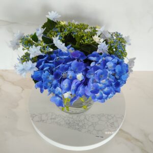 Blue and white hydrangea bouquet in a glass vase on marble surface.