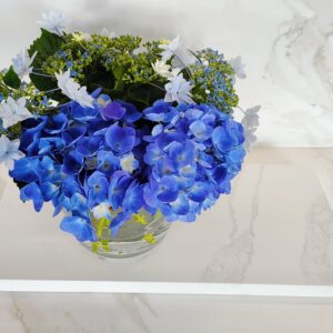 Blue hydrangeas in a glass vase on marble surface.