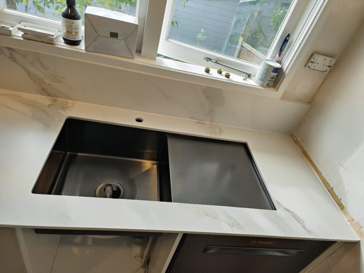 Modern kitchen sink with marble countertop and window view.