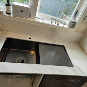 Modern kitchen sink with marble countertop and window view.