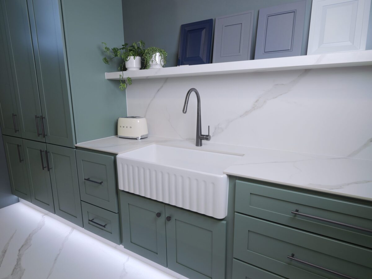 Modern kitchen with green cabinets, white countertop, and farmhouse sink.