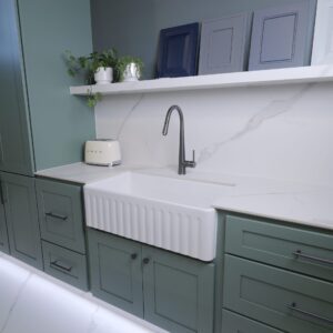 Modern kitchen with green cabinets, white countertop, and farmhouse sink.