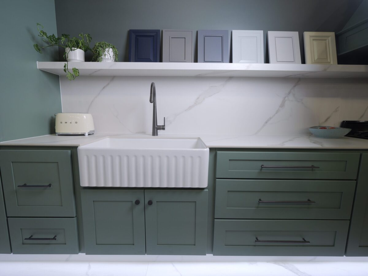 Modern kitchen with green cabinets, white sink, and decorative frames on shelf.