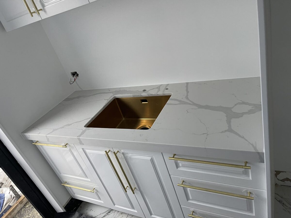 White kitchen countertop with gold sink and handles.