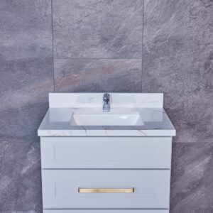 White bathroom vanity with marble countertop and gold handles against gray tile wall.