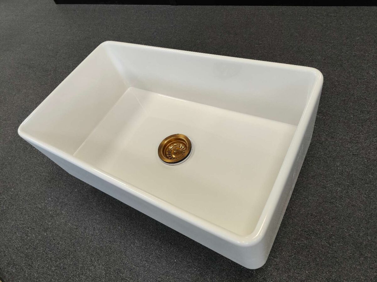 White rectangular kitchen sink with a gold drain on dark countertop.
