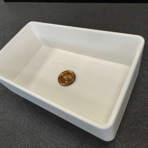 White rectangular kitchen sink with a gold drain on dark countertop.