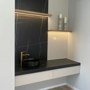 Modern bathroom vanity with black sink and gold faucet.