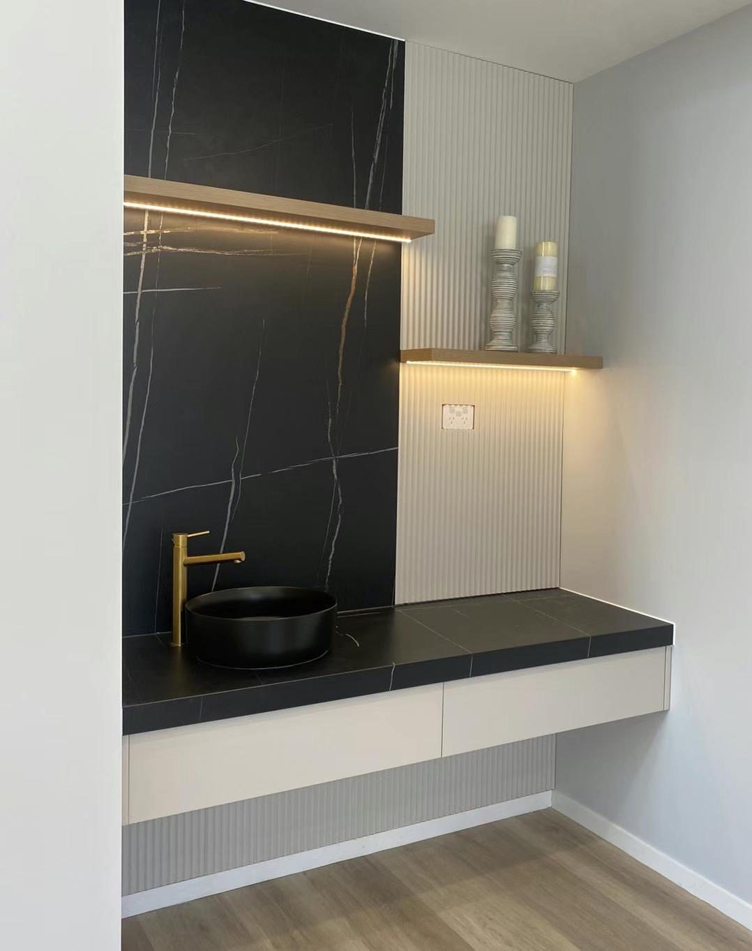 Modern bathroom vanity with black sink and gold faucet.