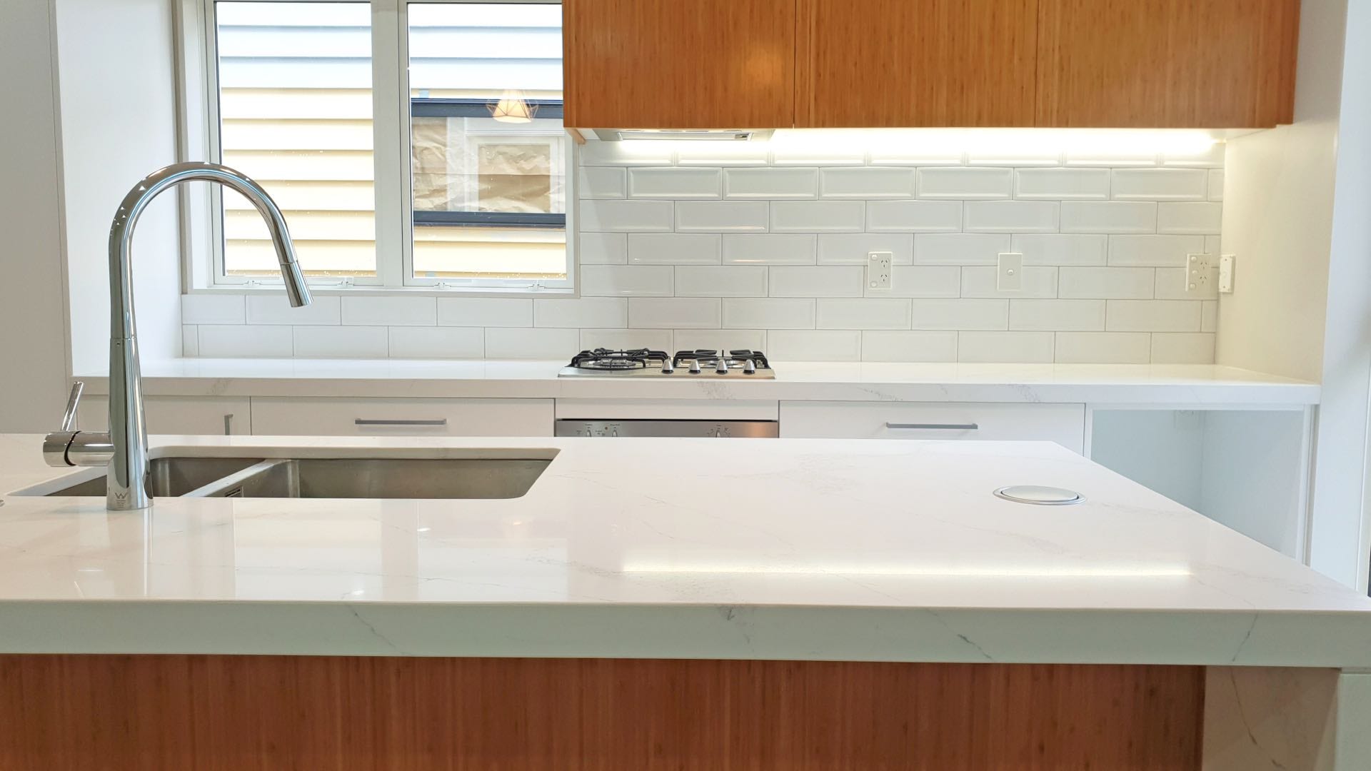 Modern kitchen with white marble countertop and wooden cabinets.