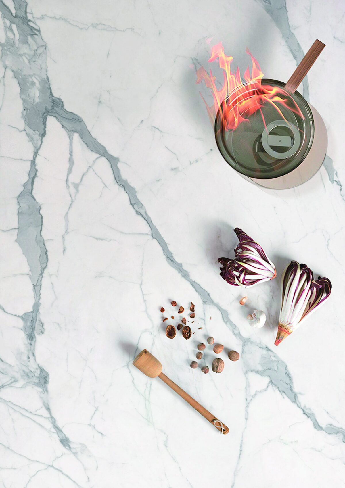 Marble countertop with vegetables, spices, and a flaming pot.