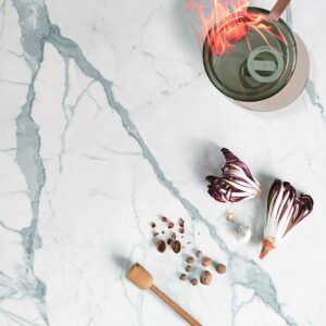 Marble countertop with vegetables, spices, and a flaming pot.